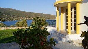 A building with yellow columns and a white facade, overlooking a body of water and hills. - Villa Axia-Art 5pm from the sea (Evia)