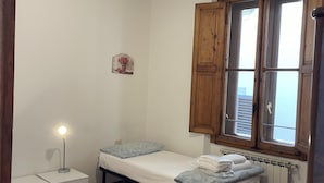 A small, tidy room with two single beds, a nightstand, a lamp, and a window with wooden shutters. - Scarlatti in Florence (Florence)