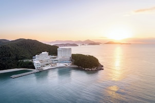 Un hotel costero de diseño moderno, ubicado en una pequeña isla con vistas al mar y montañas a lo lejos.