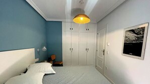 A bedroom with a bed, a wardrobe, a chair, and a hanging light fixture. - Apartamento La Peatonal (Hervás)