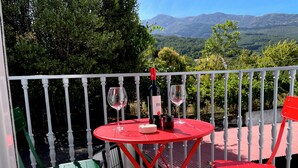 A red table with two wine glasses and a bottle on a balcony with white railings, overlooking a mountainous landscape. - Apartamento La Peatonal (Hervás)