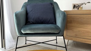 A teal armchair with a striped pillow, a wooden sideboard, and a framed abstract painting on the wall. - Apartamento La Peatonal (Hervás)