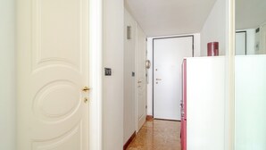 Un corridoio stretto con una porta bianca a sinistra, una porta bianca in fondo e un frigorifero a destra.