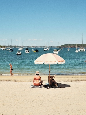 A beach with a sandy shore, a large umbrella, and several boats in the water.
