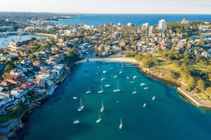 An aerial view of a coastal town with a marina filled with sailboats, surrounded by residential buildings and a clear view of the sea.
