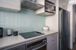 A modern kitchen with a built-in microwave, stainless steel refrigerator, and a black induction cooktop.