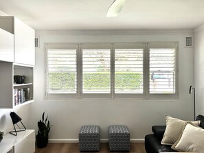 A living room with a large window, a black leather sofa, a white side table, and a black floor lamp.