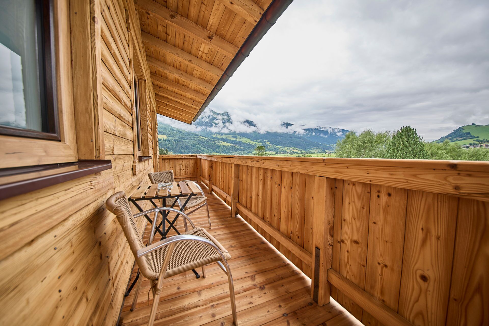 A wooden deck with a table and chairs, overlooking a mountainous landscape.