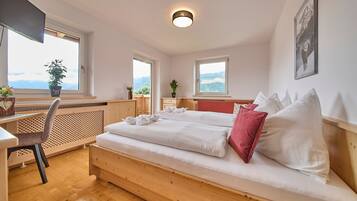 Ein Schlafzimmer mit Bett, Schreibtisch und Stuhl. Es gibt Fenster mit Blick ins Freie.