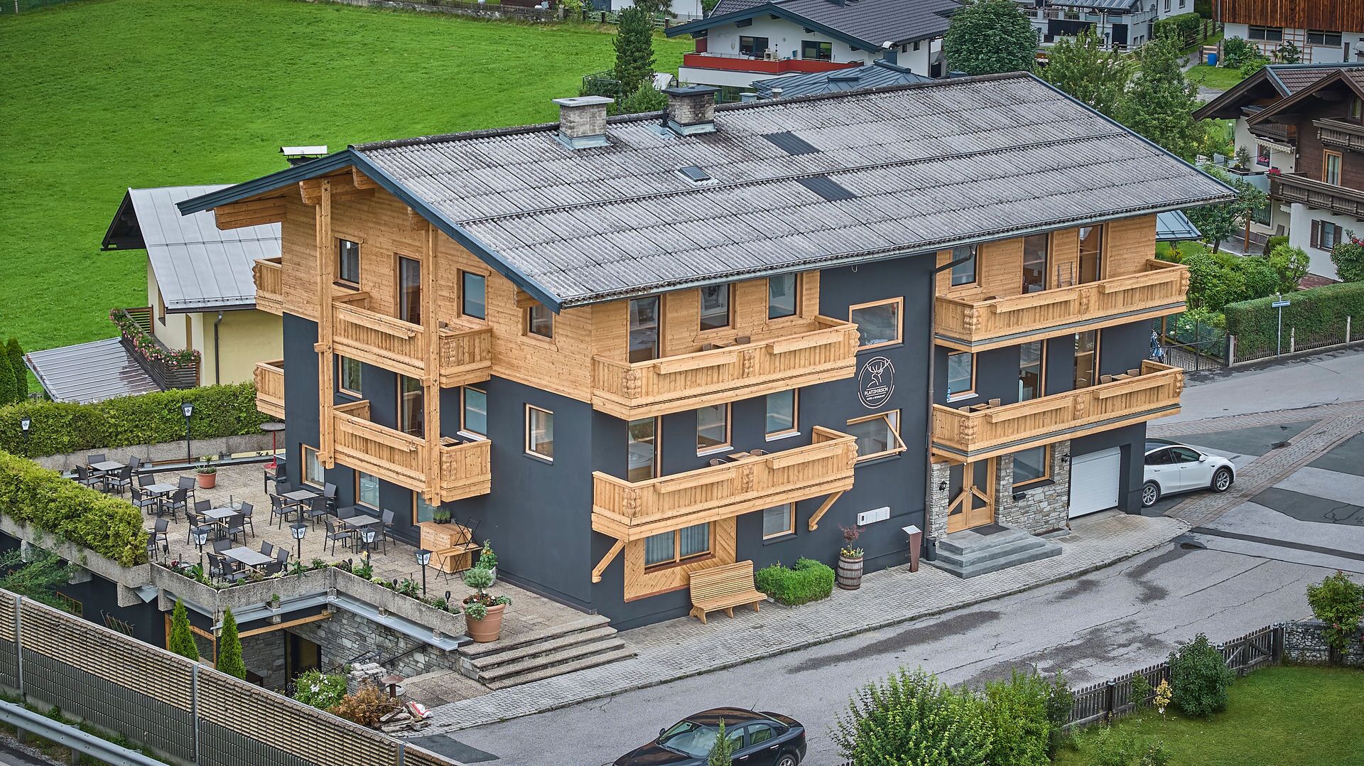 Een meerlaags gebouw met houten balkons, een gevel van natuursteen en een geplaveid terras met buiten zitplaatsen.
