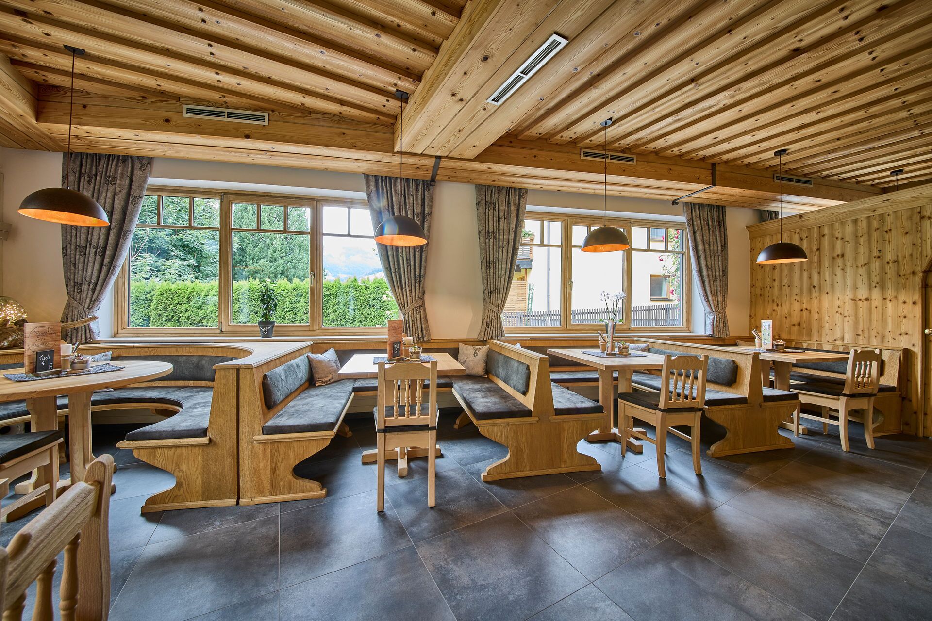 Un restaurante acogedor con bancos y mesas de madera, amplios ventanales que ofrecen vistas a la vegetación y un alto techo de madera.