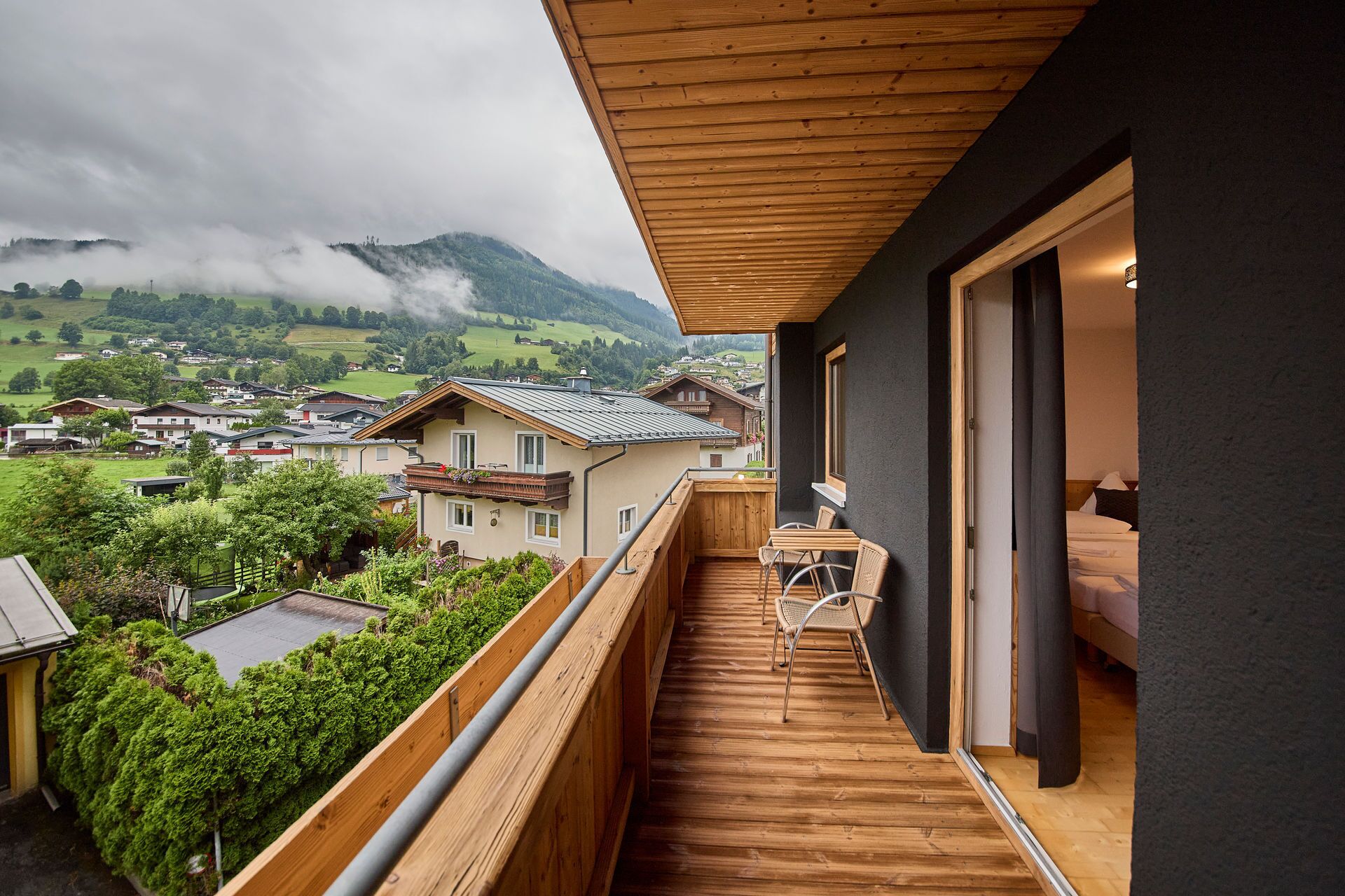 Ein Balkon mit Holzboden, Tisch und Stühlen mit Blick auf ein Dorf und Berge.
