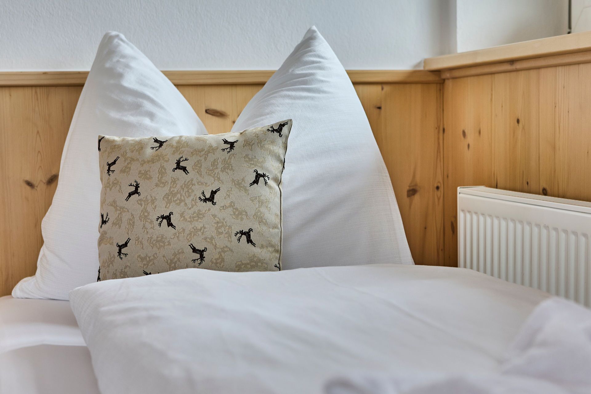 Una cama con sábanas blancas y dos almohadas, una lisa y otra con estampado de ciervo.