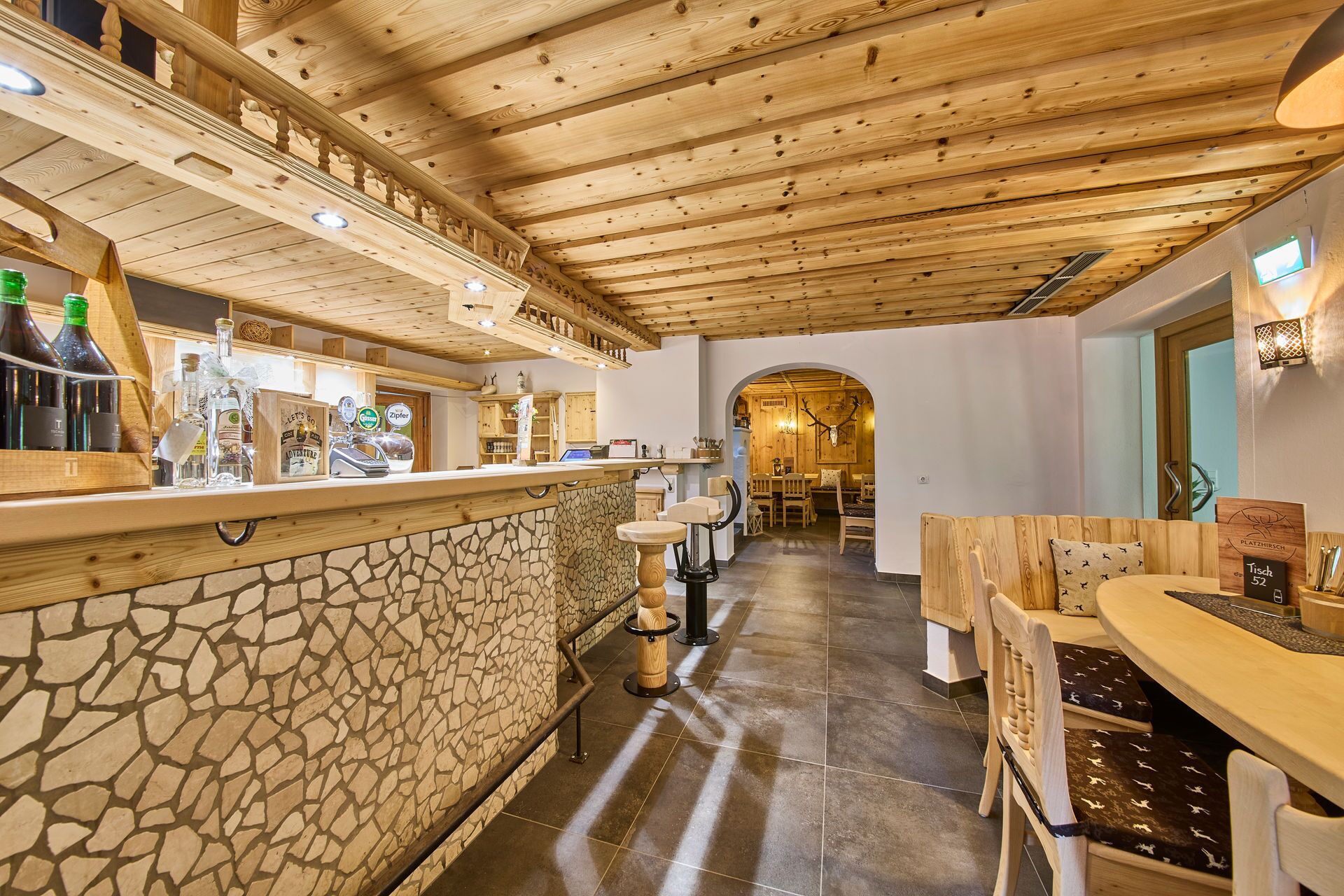Eine Bar mit Holzbalken und Steindekoration, ein Sitzbereich mit Tischen und Stühlen sowie ein Blick in einen Essraum.