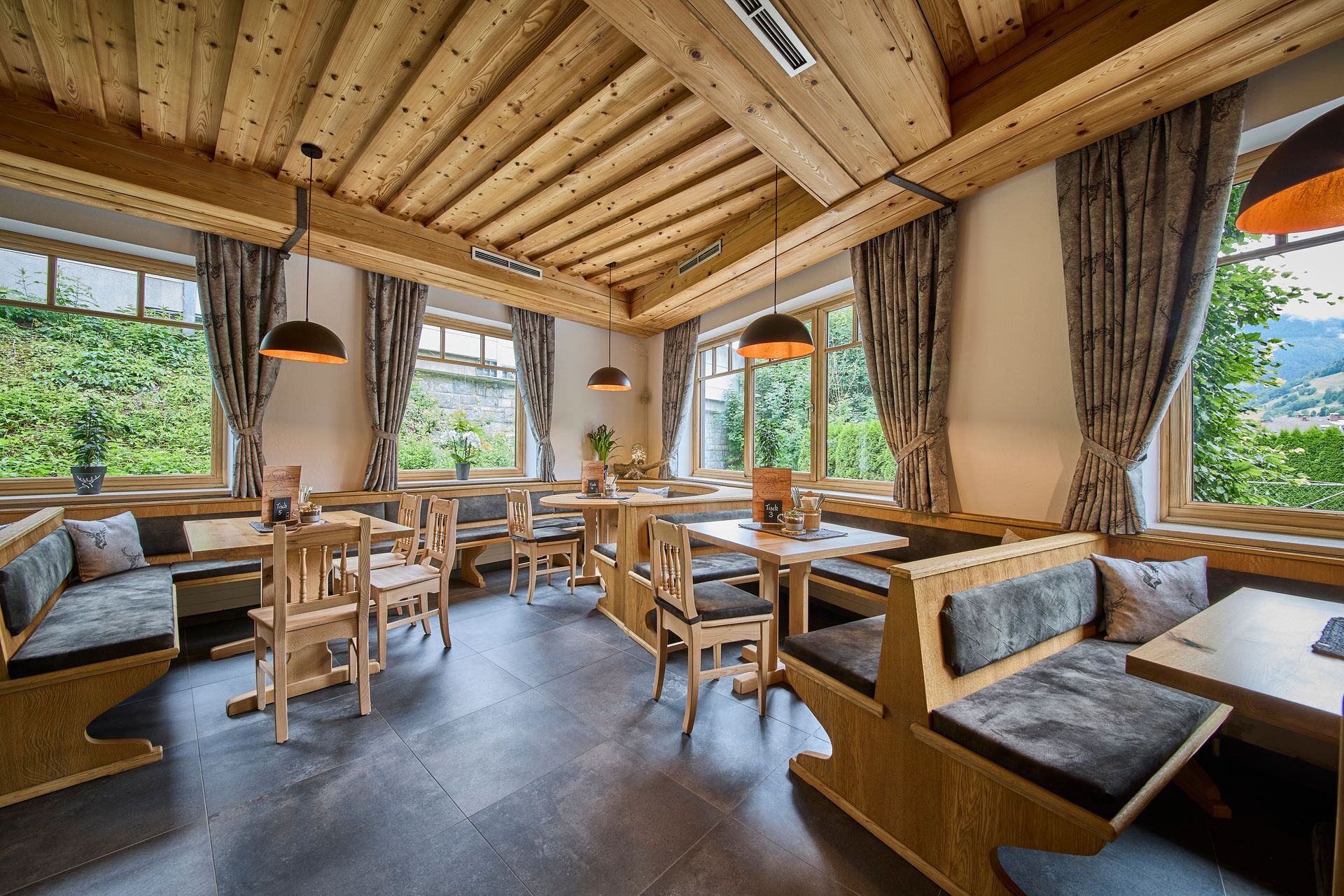 Un restaurant chaleureux, doté de meubles en bois, de grandes fenêtres et offrant une vue sur la verdure.