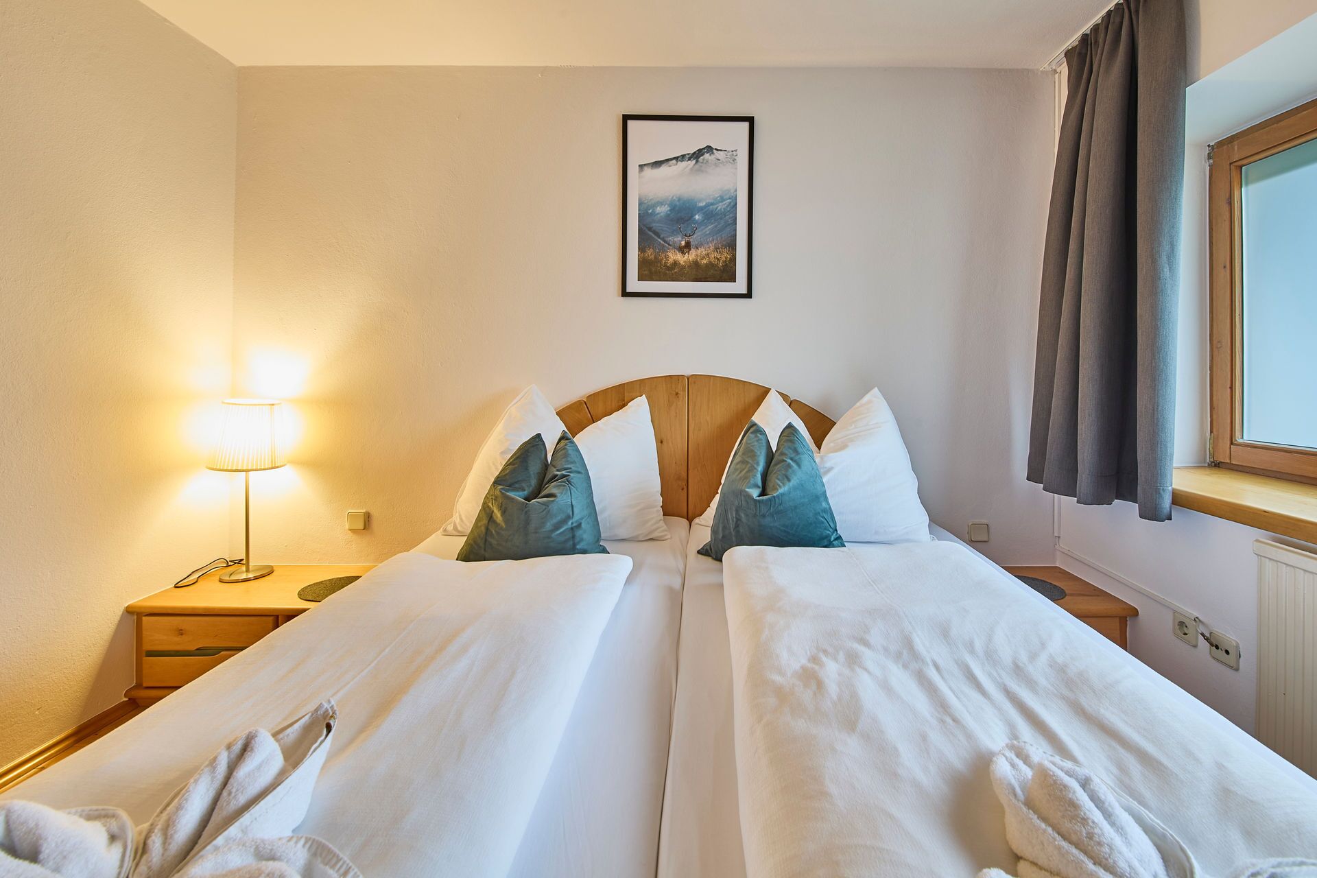 Habitación de hotel con dos camas, una lámpara de noche, un cuadro en la pared y una ventana con cortinas.