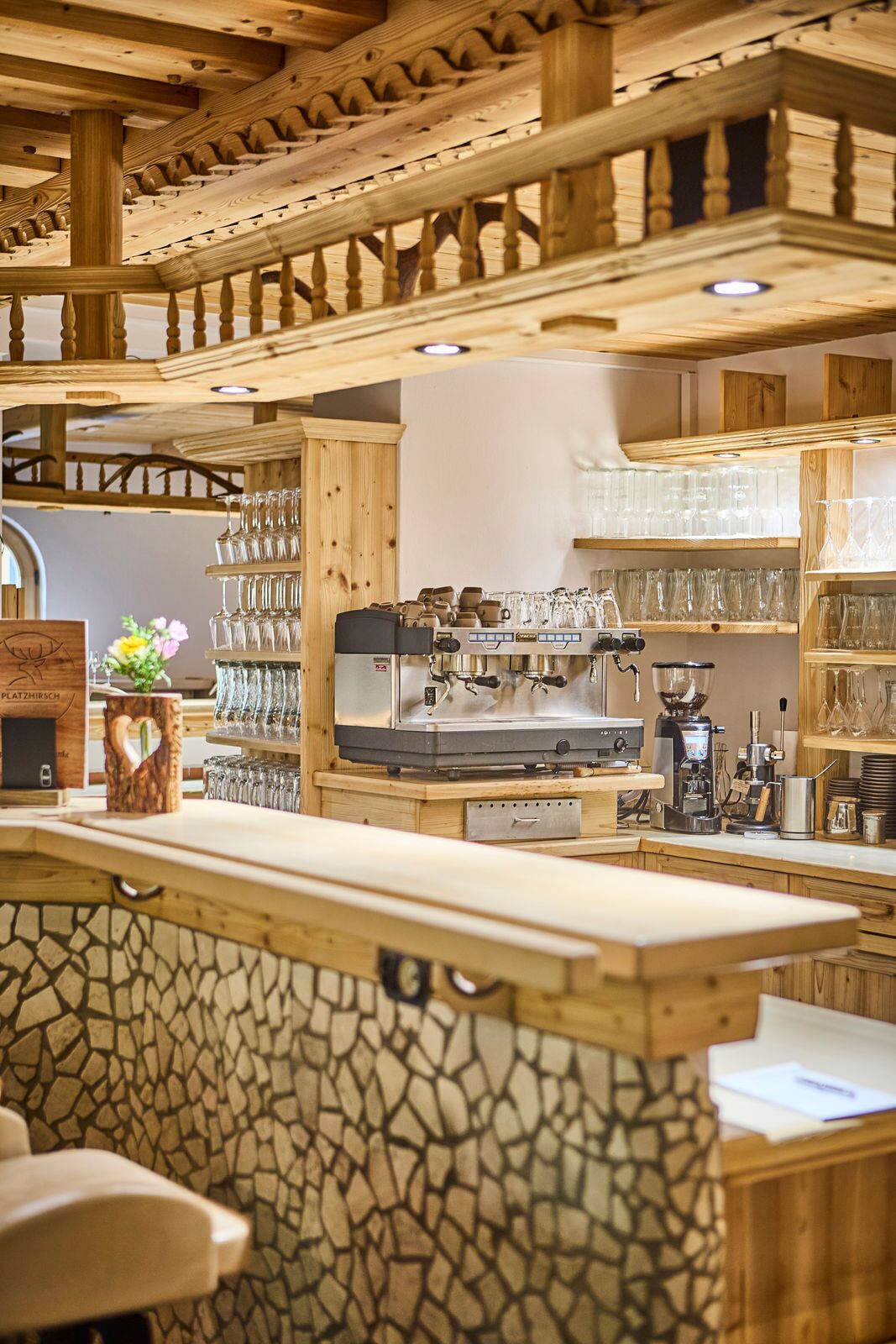 Ein Holzinterieur mit einer Steinarbeitsplatte, einer Kaffeemaschine und Regalen mit Gläsern.