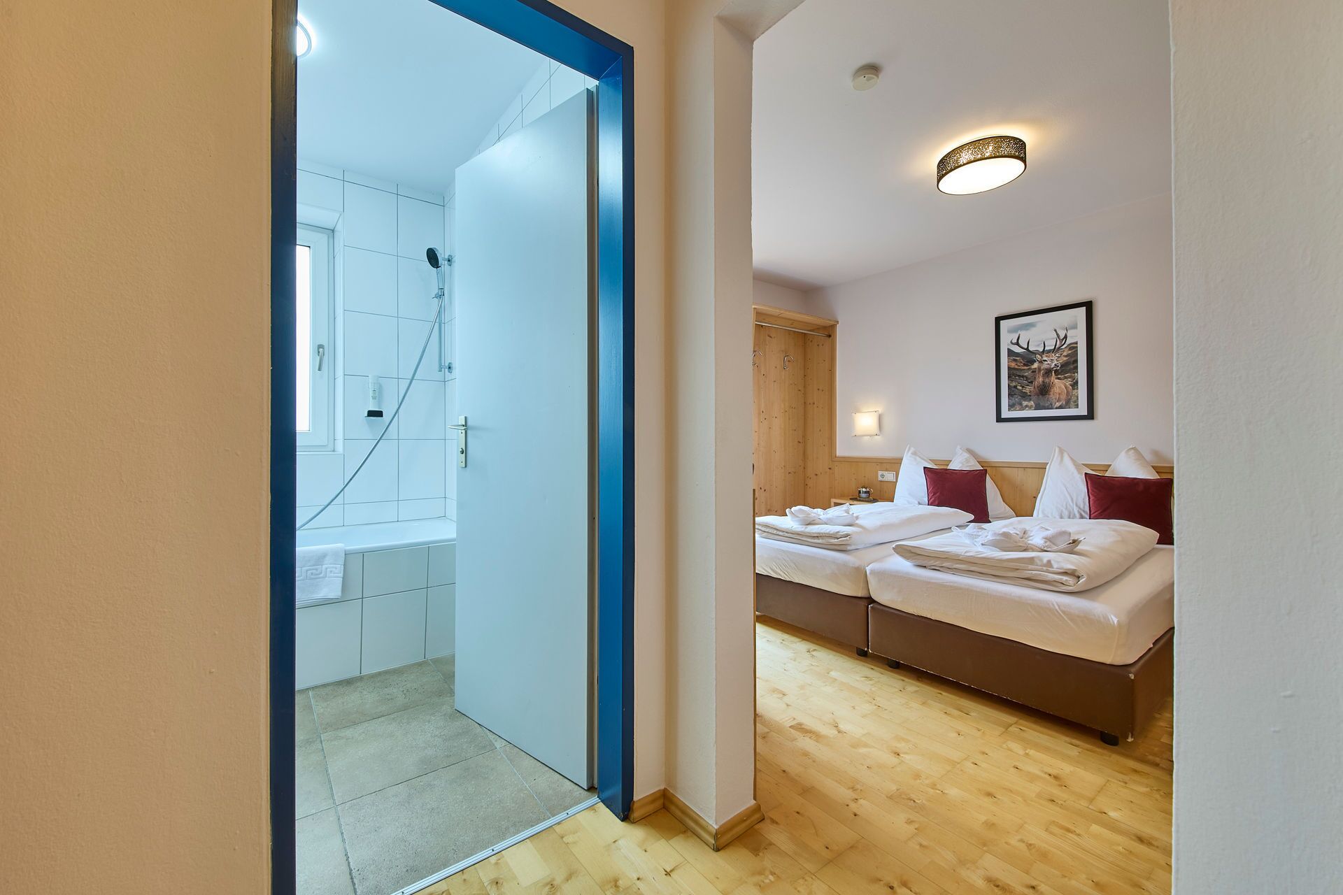 Habitación de hotel con piso de madera, ducha, cama con almohadas rojas y un cuadro enmarcado en la pared.