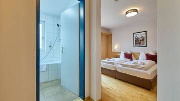 Habitación de hotel con piso de madera, ducha, cama con almohadas rojas y un cuadro enmarcado en la pared.