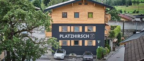 Un edificio de dos pisos con un letrero que dice "PLATZHIRSCH" y un coche estacionado adelante.