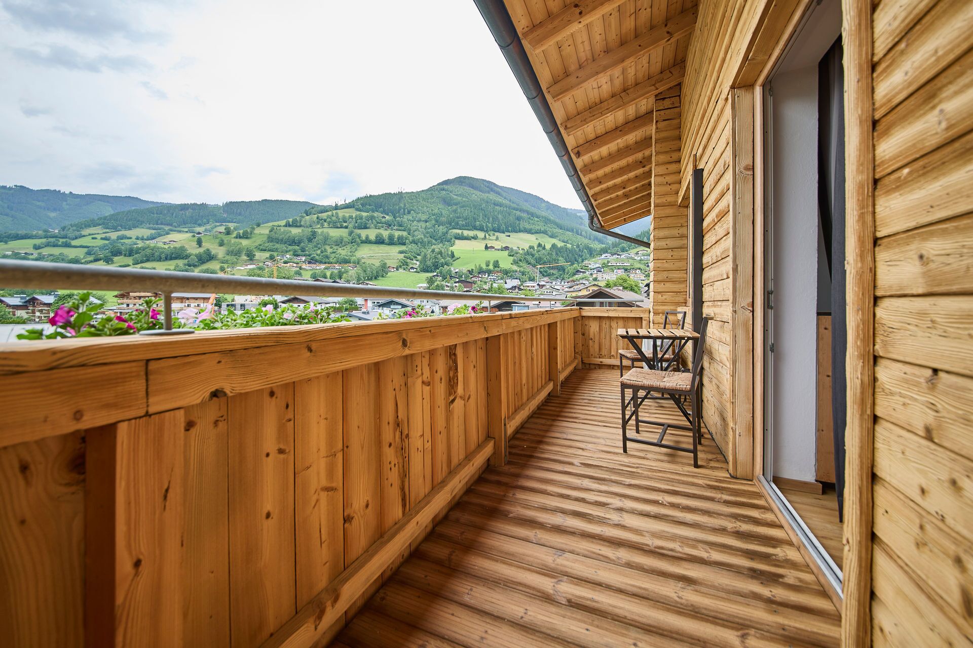 A wooden balcony with a view of a green valley and mountains.