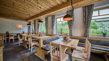 A restaurant with wooden tables and benches, large windows with curtains, and pendant lighting.