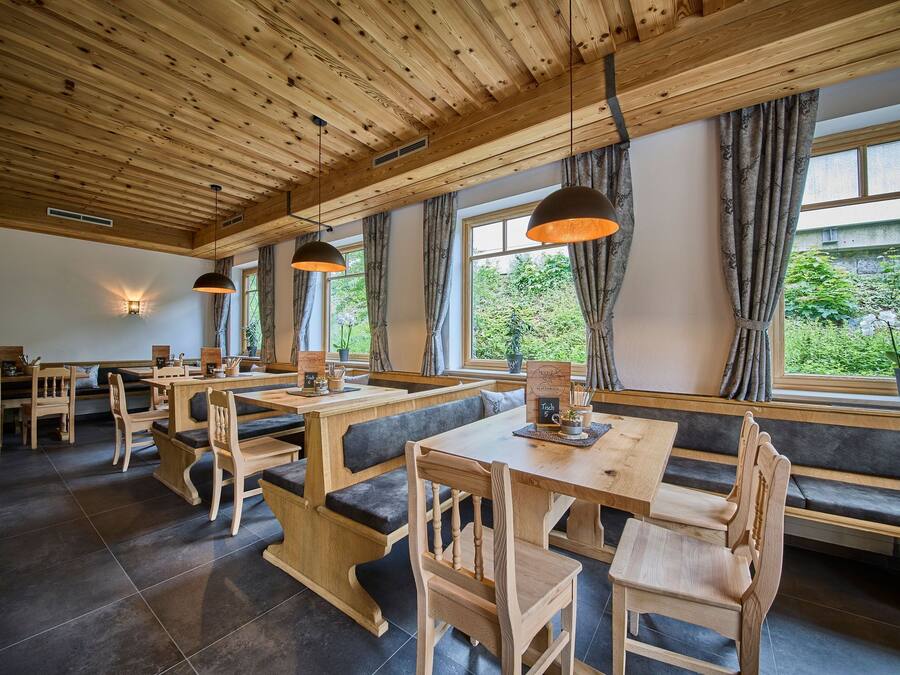 A restaurant with wooden tables and benches, large windows with curtains, and pendant lighting.