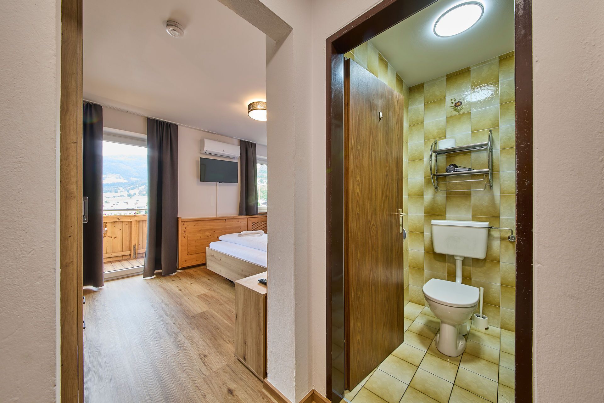 Une chambre d’hôtel avec un lit en bois, une télévision et une salle de bain équipée de toilettes et d’une étagère.