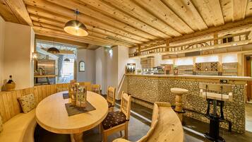 Un interior acogedor de madera con una mesa redonda para comer, sillas de madera, una pared de acento de piedra y una zona de bar con estantes llenos de vasos y botellas.