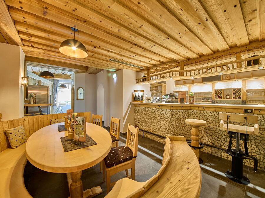 Un interior acogedor de madera con una mesa redonda para comer, sillas de madera, una pared de acento de piedra y una zona de bar con estantes llenos de vasos y botellas.