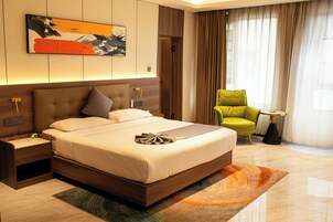 Una habitación de hotel moderna con una cama grande, una mesita de noche, un sillón verde y un cuadro en la pared.