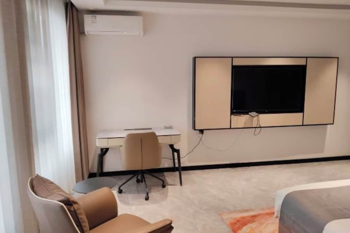 A hotel room with a bed, a desk, a chair, and a television mounted on the wall.