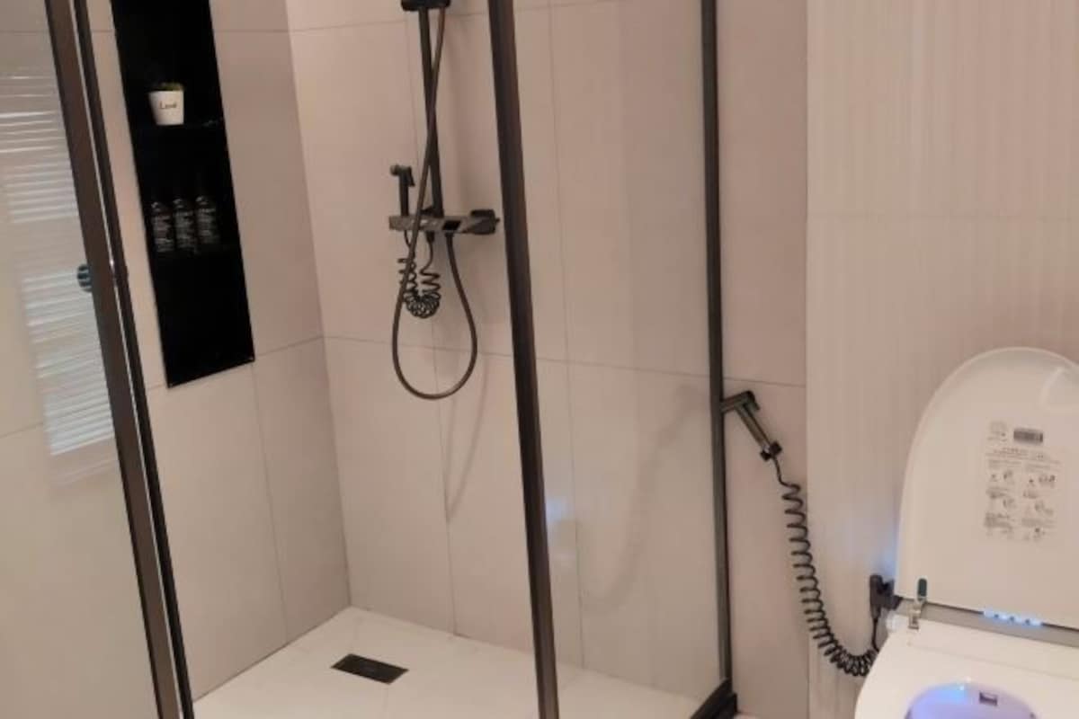 A shower area with a glass door, a handheld showerhead, and a wall-mounted control panel.