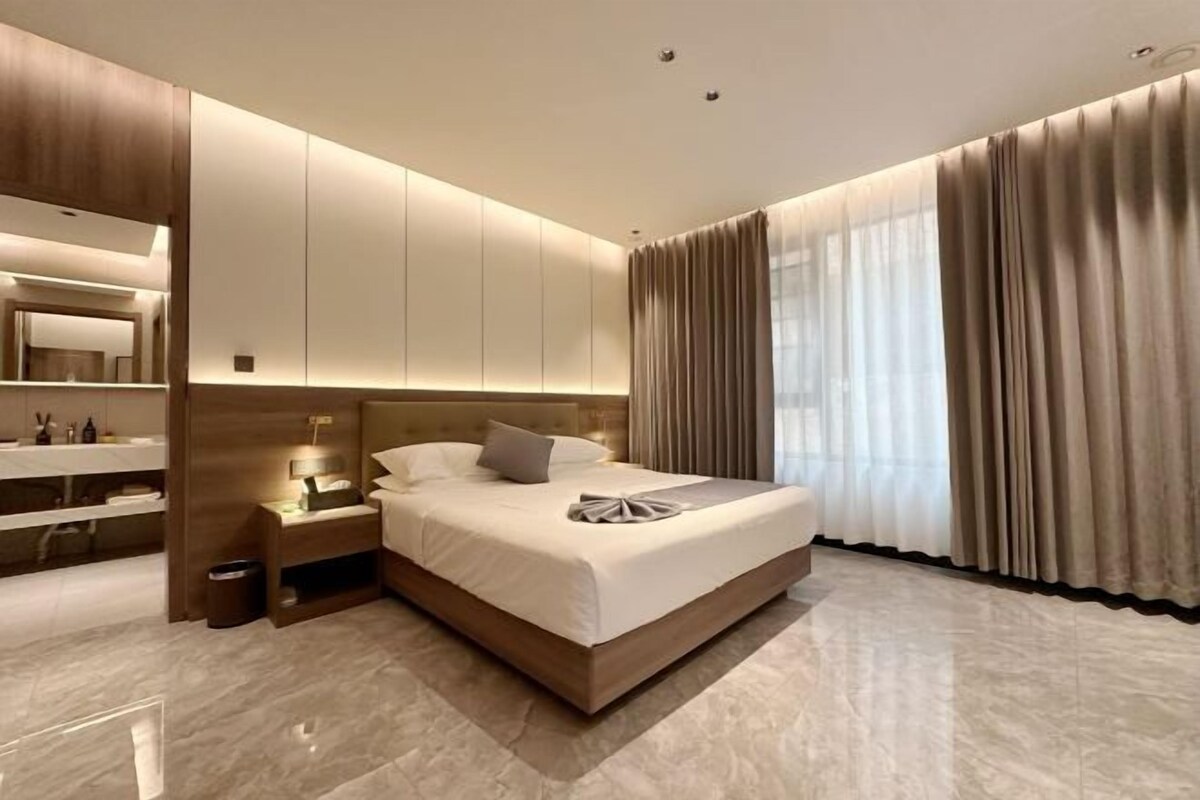 A modern hotel room with a large bed, a bedside table, a nightstand, and a built-in wardrobe.