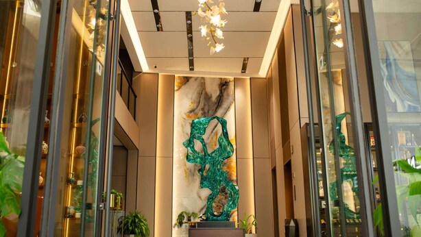 A modern lobby with glass walls, a marble wall with a green glass sculpture, and potted plants. - Eden Hotel  (Kinshasa)