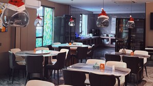 A modern dining area with round tables and chairs, a kitchen in the background, and decorative Santa hats hanging from the ceiling. - Eden Hotel  (Kinshasa)