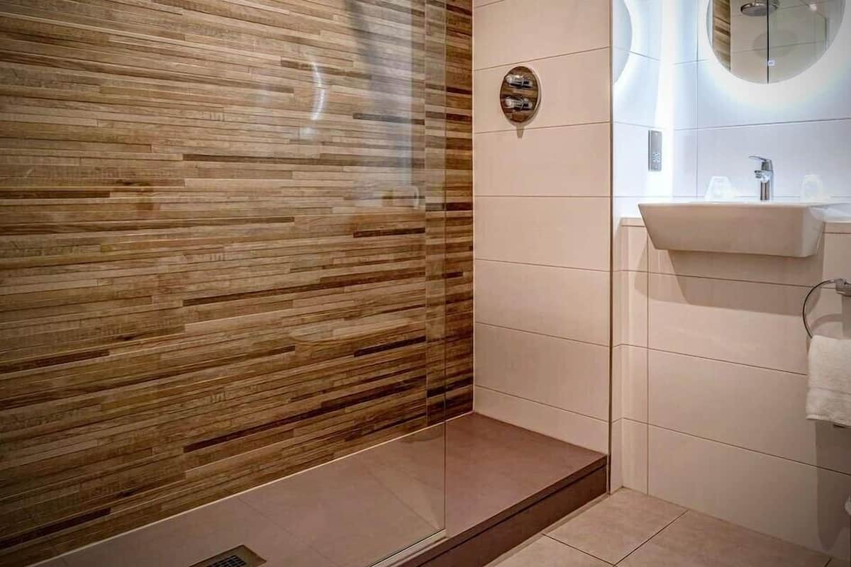 A modern bathroom with a wooden wall, a glass shower enclosure, and a sink with a mirror.