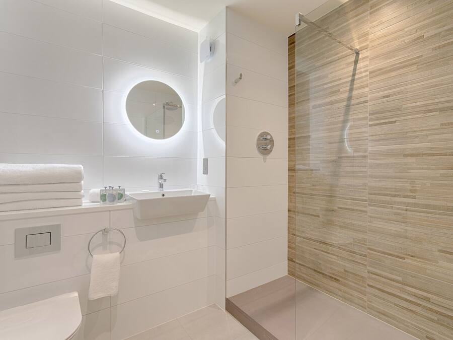 A modern bathroom with a glass-enclosed shower, a round mirror, and a white sink.