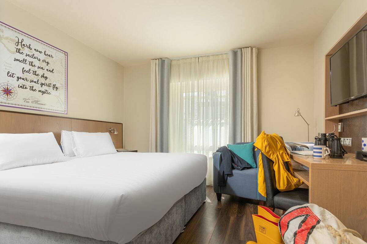 A hotel room with a large bed, a desk with a chair, a television, and a window with curtains.