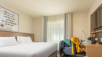 Una habitación de hotel con una cama grande, un escritorio con silla, televisor y una ventana con cortinas.