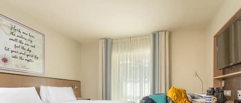 Una habitación de hotel con una cama grande, un escritorio con silla, televisor y una ventana con cortinas.