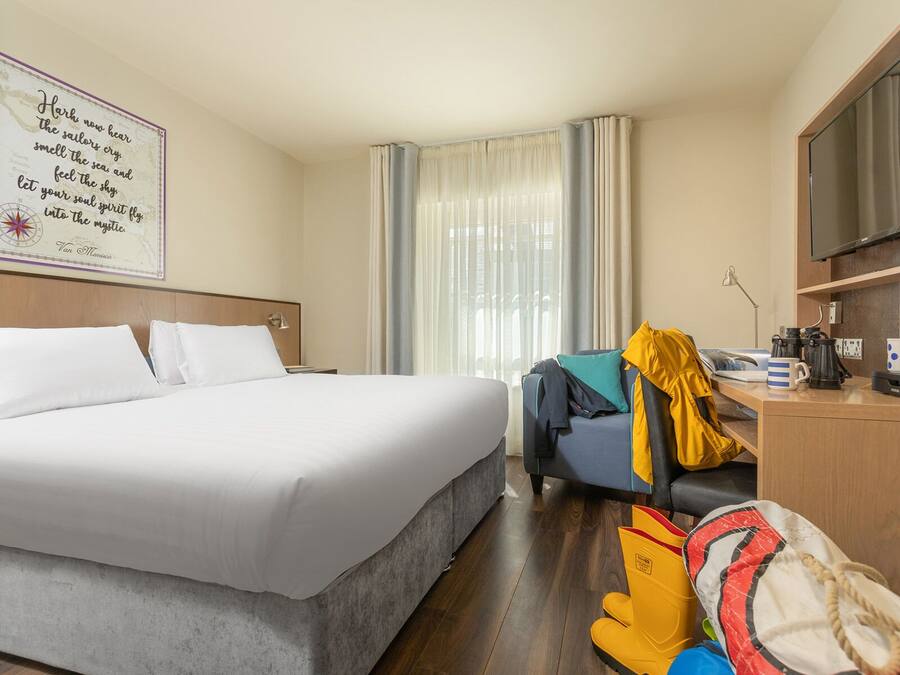 Ein Hotelzimmer mit einem großen Bett, einem Schreibtisch mit Stuhl, einem Fernseher und einem Fenster mit Vorhängen.