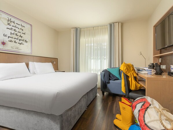 A hotel room with a large bed, a desk with a chair, a television, and a window with curtains. - The Mariner Hotel (Westport)