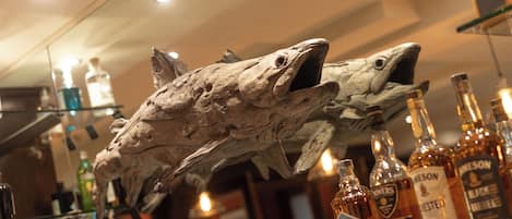 A bar area with a large fish sculpture, various liquor bottles, and a mirror reflecting the space.