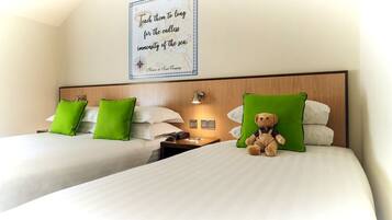 Habitación de hotel con dos camas, almohadas verdes, un cartel en la pared y un peluche sobre una de las camas.