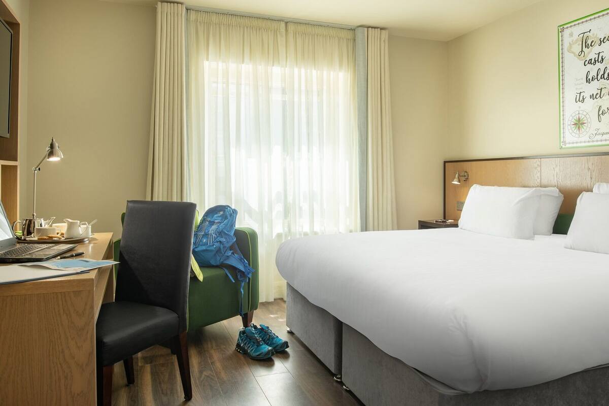 A hotel room with a bed, desk, chair, and a window with curtains.