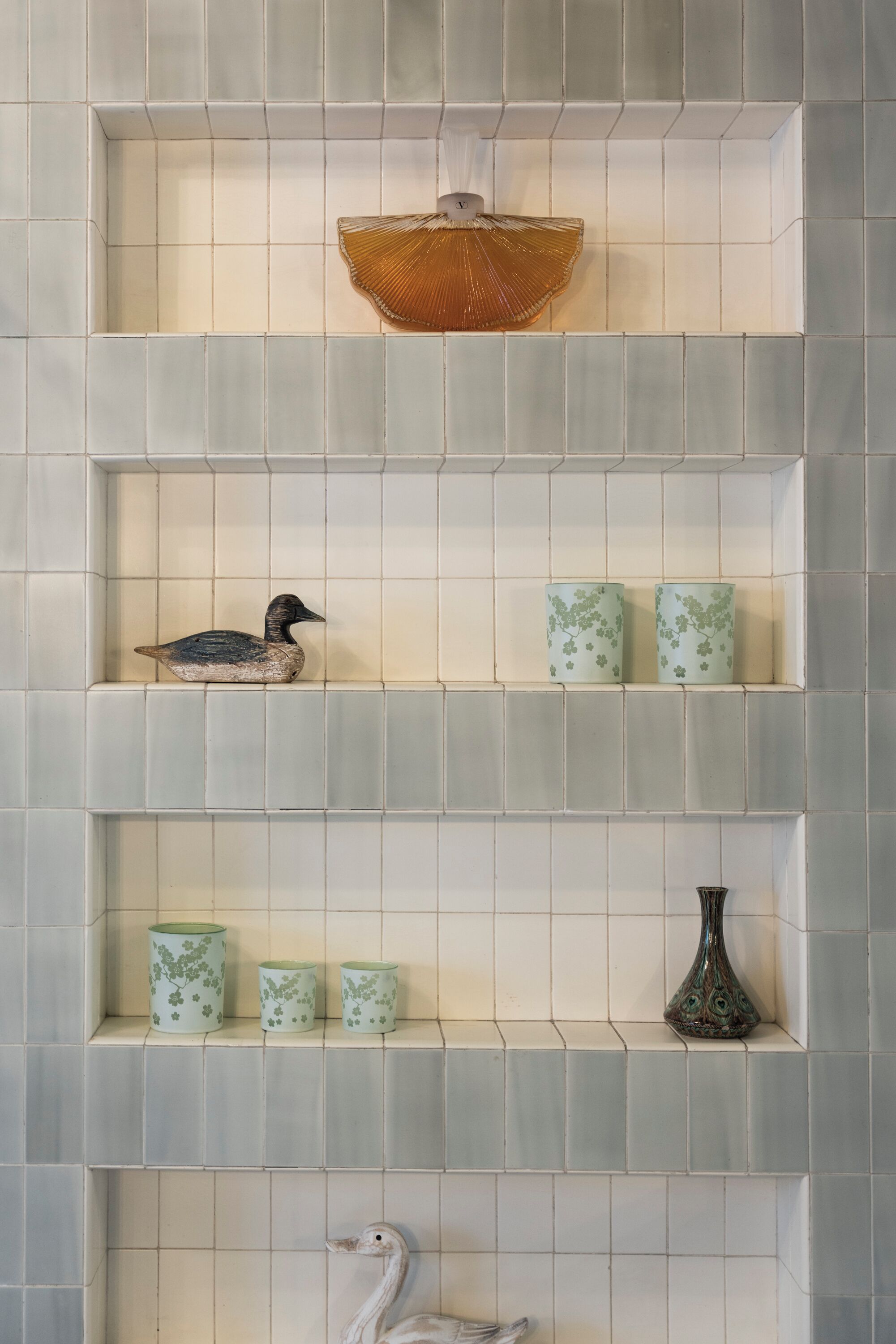 A tiled wall with shelves holding decorative items including a duck, two floral vases, and a basket.