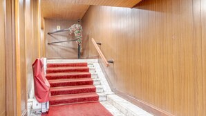 Eine Holztreppe mit roten Teppichstufen und einem Geländer, die zu einer Zwischenebene mit einer Holzwand und einer Blumenkomposition führt.
