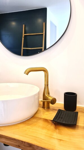 Bathroom features a large sink, gold faucet, and a round mirror with a gold frame.