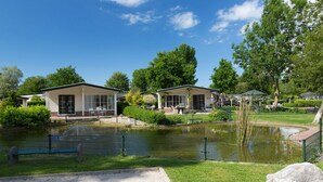 A tranquil park with a pond, two small buildings, and a large rock in the foreground. - Nice Tent With Bathroom, Near a Recreation Area (Noord-Scharwoude)
